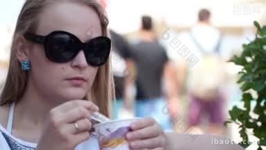 近距离的肖像年轻女子戴着太阳镜吃冰淇淋在街头咖啡馆